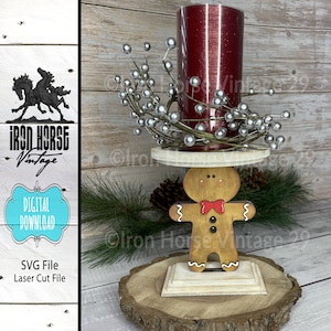 May include: A wooden gingerbread man candle holder with a red candle and silver berry sprigs. The candle holder is on a wooden base.