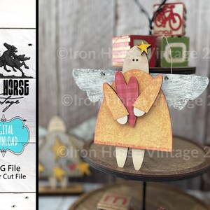 May include: A wooden angel ornament with a heart in its hands. The angel is painted in shades of yellow, orange, and red. The wings are painted white with a distressed look. The ornament is hanging from a string.