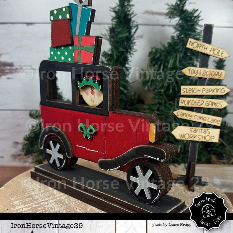 May include: A wooden Christmas decoration of a red vintage car carrying a stack of wrapped gifts and a smiling elf. The car is on a wooden base and there is a wooden signpost with the words "North Pole", "Toy Factory", "Sleigh Parking", "Reindeer Games", "Candy Cane Lane", and "Santa's Workshop" on it.