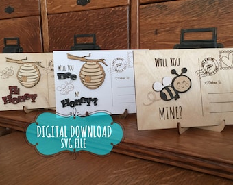 May include: Three wooden postcards featuring bee-themed designs. The first postcard reads "Hi Honey" with a beehive and a bee. The second postcard reads "Will you bee my honey?" with a beehive and a bee. The third postcard reads "Will you bee mine?" with a bee and a heart.