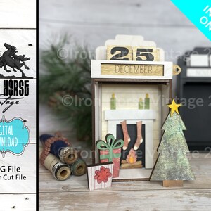 以下が含まれることがあります： 「12月25日」と書かれたカレンダーのある木製のクリスマス暖炉のシーン。暖炉にはマントルから靴下がかかっており、暖炉には火が燃えています。暖炉の右側に小さなクリスマスツリーがあります。