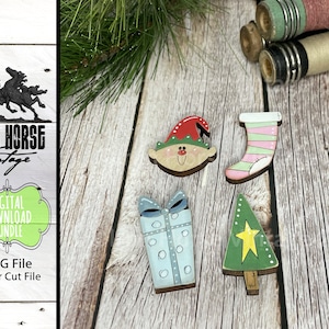 May include: A set of five Christmas-themed wooden ornaments. The ornaments are painted in various colors, including red, green, blue, pink, and white. The ornaments depict a Christmas tree, a gift box, a stocking, an elf, and a star.