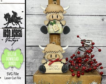 May include: Two wooden Christmas ornaments shaped like Highland cows. The first ornament has the text "FOR MOO" on it. The second ornament has the text "MOOEY CHRISTMAS" on it.
