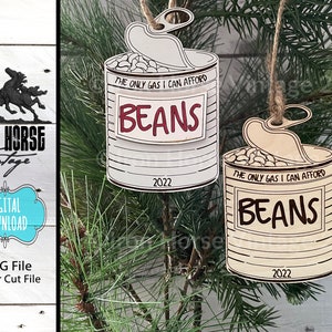 May include: Two wooden Christmas ornaments shaped like cans of beans. The cans are decorated with the text "The only gas I can afford" and "Beans". The year 2022 is printed on the bottom of each can.
