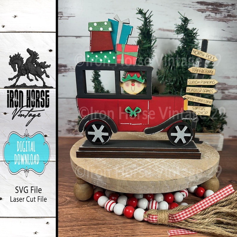 May include: Red wooden toy car with a Christmas elf driver, carrying a stack of wrapped gifts. The car is on a wooden base with a sign that reads "North Pole Toy Factory" and other Christmas-themed signs.