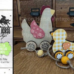 May include: A wooden pull toy set featuring a brown and white checkered hen and a yellow and white checkered chick. The hen has a red comb and a pink and white patterned wing. The chick has an orange beak and a small orange spot on its chest. Both toys have wheels and are connected by a string.