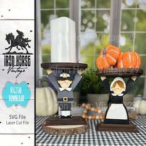 May include: Two wooden candle holders featuring pilgrim figures holding trays. One figure is holding a white candle and the other is holding two orange pumpkins.