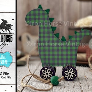 May include: A wooden toy dinosaur with green and black checked pattern, on wheels with white flower designs. The dinosaur has a pull string and a green bead.