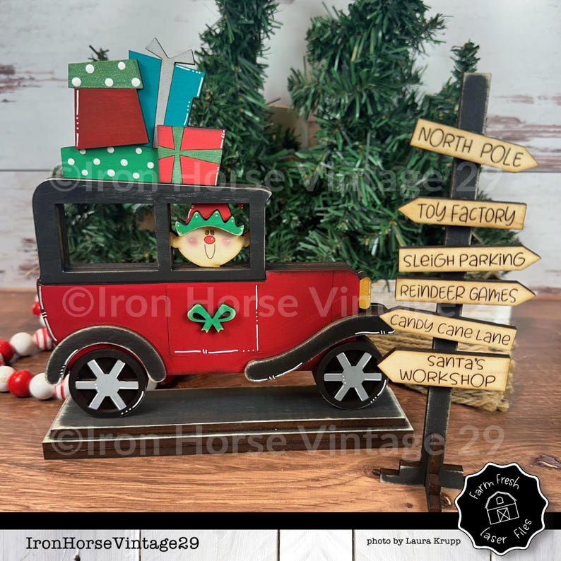 May include: A red wooden toy car with a black roof and a smiling elf driver. The car is carrying a stack of wrapped gifts. A wooden signpost with arrows points to various locations in Santa's workshop, including the North Pole, Toy Factory, Sleigh Parking, Reindeer Games, Candy Cane Lane, and Santa's Workshop.