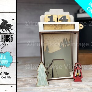 May include: A wooden calendar with a camping theme. The calendar is set to July 14th. The calendar has a small tent, a pine tree, and a lantern.