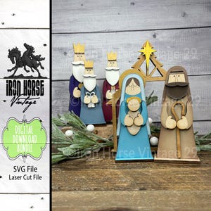 May include: Wooden nativity scene featuring figures of the Three Wise Men, Mary, Joseph, and baby Jesus. The figures are painted in various colors, including blue, purple, and brown. The scene includes a wooden star and a stable. The image also includes the text "IRON HORSE Vintage".