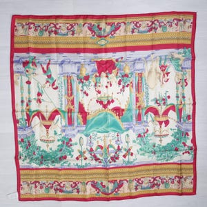 Pu&ograve; includere: Una sciarpa quadrata di seta con un design dettagliato e ornato. La sciarpa presenta una scena centrale con un letto e composizioni floreali, incorniciata da un bordo rosso ed elementi decorativi in oro, verde e blu. L'estetica generale &egrave; elegante e vintage.