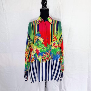 May include: A button-down shirt with a vibrant floral and striped design. The shirt features a red center panel, green and yellow stripes, and a white and navy blue striped bottom. The long-sleeved shirt is displayed on a black mannequin.