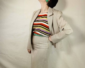 May include: A white and black striped skirt suit with a colourful striped top. The jacket has a notched collar and long sleeves. The skirt is a pencil skirt with a zip closure. The top has a scoop neck and short sleeves.
