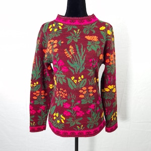 Peut inclure: Un pull bordeaux à motifs floraux. Le pull a un col montant et des manches longues. Le motif floral comprend des fleurs et des feuilles roses, jaunes, oranges et vertes. L'encolure et l'ourlet sont bordés d'une bordure rose.