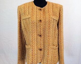 May include: A golden-yellow tweed jacket with a round neckline and long sleeves. The jacket features two front pockets and three brown buttons down the front. The tweed fabric has a textured appearance with flecks of red and brown.