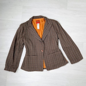 May include: A brown and black plaid blazer with a single button closure and a brown lining. The blazer has a slightly fitted silhouette and long sleeves.