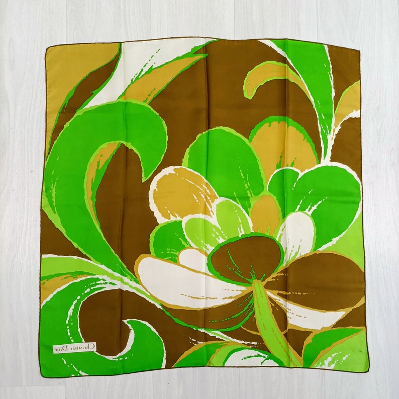 Op de afbeelding: Een bruine, groene en witte zijden sjaal met een bloemenmotief. De sjaal heeft een label met de tekst "Christian Dior".