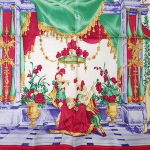 Pu&ograve; includere: Foulard di seta bianco con un'illustrazione dettagliata di una scena classica. Il design presenta figure in abiti rinascimentali, che suonano strumenti, circondate da composizioni floreali ed elementi architettonici ornati in rosso, verde e oro.