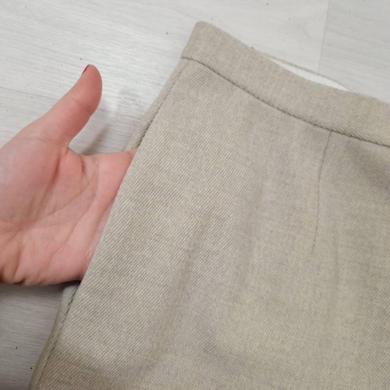 Puede incluir: Primer plano de una falda beige con un bolsillo. La tela tiene un aspecto texturizado. El bolsillo est&aacute; abierto, revelando el interior. La falda parece estar hecha de un material tejido. La prenda es probablemente parte de una colecci&oacute;n de ropa.