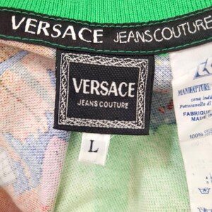 May include: Close-up of a Versace Jeans Couture shirt tag. The black tag features the brand name in white, with a decorative border. The shirt has a green collar and a colorful pattern. A white tag with text is visible.