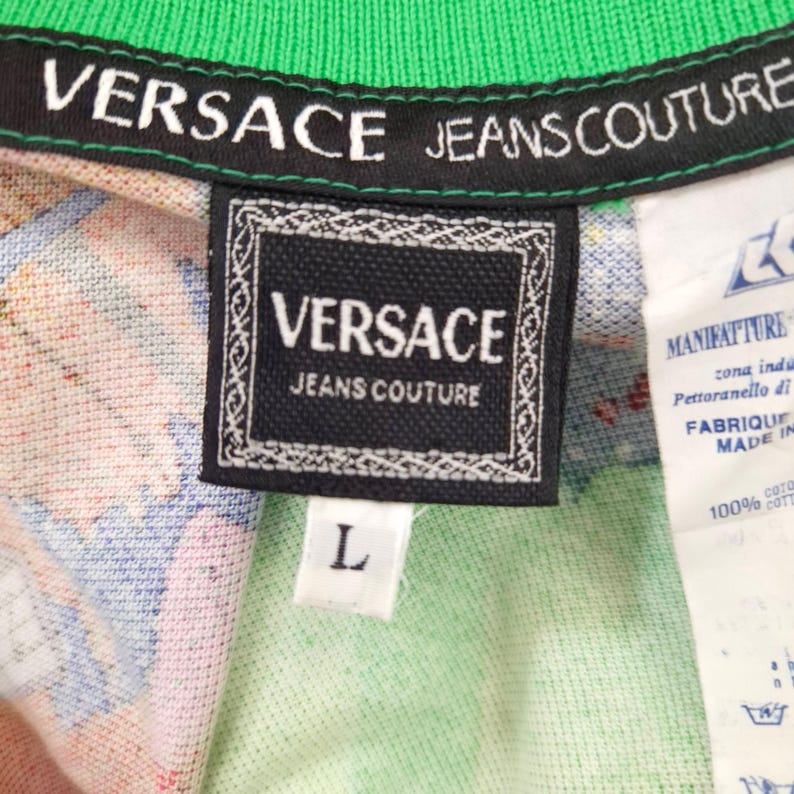May include: Close-up of a Versace Jeans Couture shirt tag. The black tag features the brand name in white, with a decorative border. The shirt has a green collar and a colorful pattern. A white tag with text is visible.