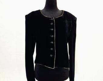 May include: A black velvet jacket with gold trim and button closure. The jacket has long sleeves and is displayed on a black mannequin. The jacket is a vintage style.