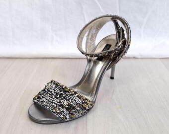 May include: Silver sequined heeled sandals with an ankle strap and buckle closure.