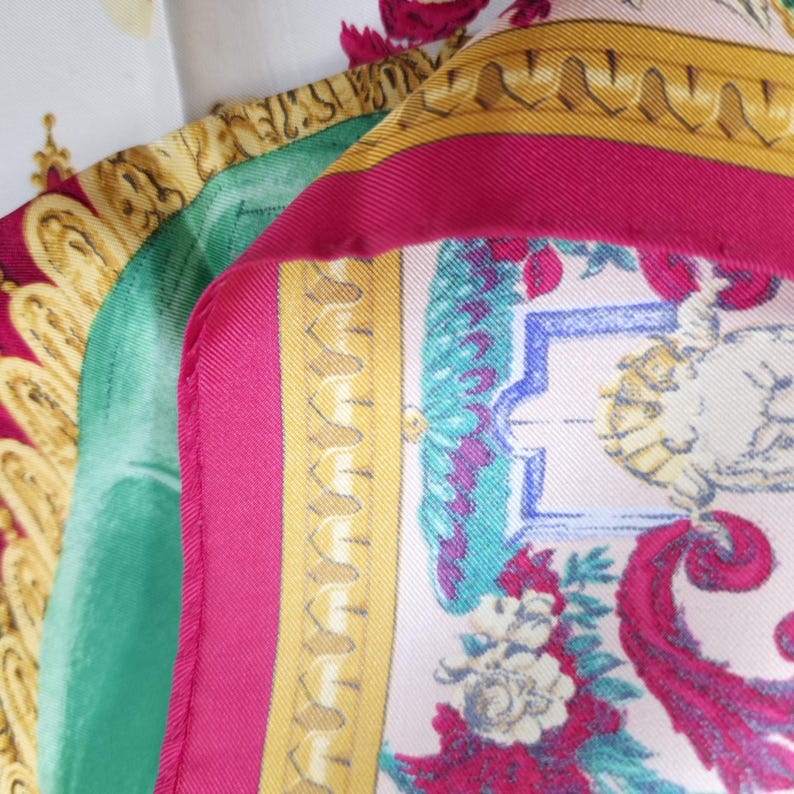 Pu&ograve; includere: Primo piano di diverse sciarpe di seta nei toni del rosa, verde e oro. Le sciarpe presentano motivi floreali e paisley ornati. Una sciarpa ha un bordo rosa e un bordo decorativo dorato.