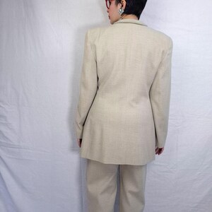 Puede incluir: Un traje de dos piezas beige, que incluye una americana y un pantal&oacute;n a juego. La americana tiene un corte entallado con hombros estructurados. El pantal&oacute;n es de pierna recta. El traje est&aacute; hecho de una tela texturizada.