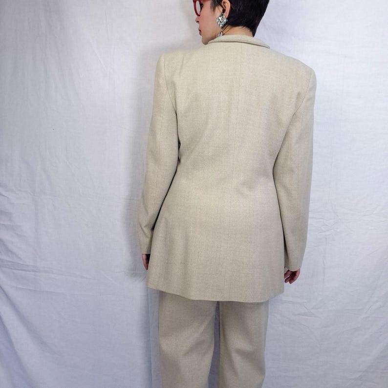 Puede incluir: Un traje de dos piezas beige, que incluye una americana y un pantal&oacute;n a juego. La americana tiene un corte entallado con hombros estructurados. El pantal&oacute;n es de pierna recta. El traje est&aacute; hecho de una tela texturizada.