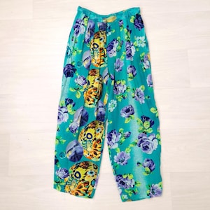 May include: High-waisted trousers in a vibrant turquoise color featuring a repeating pattern of purple and blue roses interspersed with large, detailed yellow and orange floral motifs. The pants have a relaxed, wide-leg fit with pleated details.