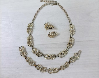 Op de afbeelding: Een gouden sieradenset met een ketting, armband en oorbellen. De sieraden hebben een bladontwerp.