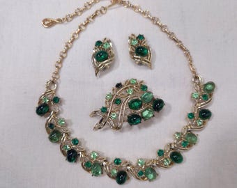 May include: A vintage green and gold tone jewelry set with a necklace, brooch, and earrings. The set features green glass stones and gold tone metal.