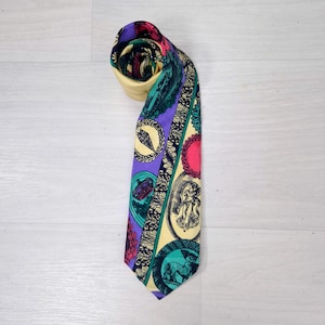 Puede incluir: Una corbata estampada con un extremo enrollado. La corbata tiene una base de color crema con diseños circulares morados, turquesa y rosas. Los diseños incluyen ilustraciones de coronas, figuras y otros elementos decorativos. La corbata está hecha de un material sedoso.