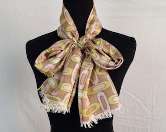 Può includere: Un foulard di seta con motivo marrone, rosa e giallo con bordo a frangia. Il foulard è legato a fiocco intorno al collo di un manichino.