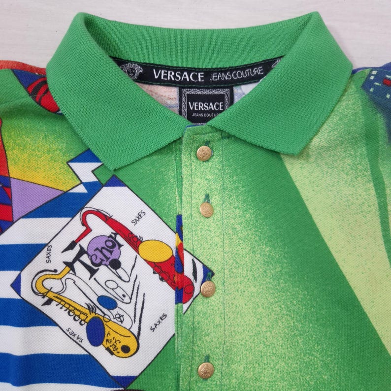 May include: A green polo shirt with a green collar and gold buttons. The shirt features a colorful abstract design with the text "Tehor" and saxophone illustrations. The collar has the "Versace Jeans Couture" logo.