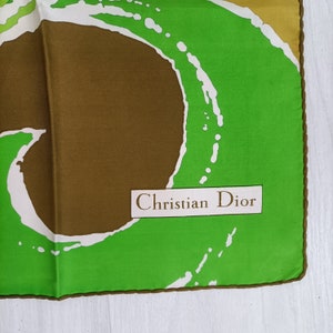 Op de afbeelding: Een groene, bruine en witte zijden sjaal met een abstract ontwerp. De sjaal heeft een label met de tekst "Christian Dior".