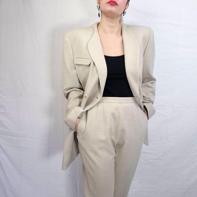 Puede incluir: Un traje de dos piezas beige, que consta de una blazer y un pantal&oacute;n a juego. La blazer tiene solapas con muescas, un cierre de un solo bot&oacute;n y un peque&ntilde;o bolsillo. El pantal&oacute;n tiene una pernera recta. El traje se lleva sobre un top negro.