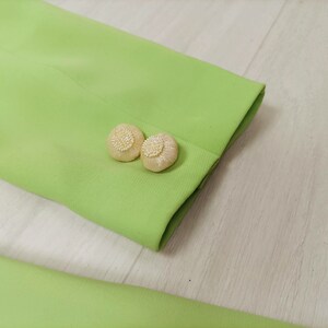 May include: Close-up of a lime green blazer with two white pearl-like buttons on the cuff.