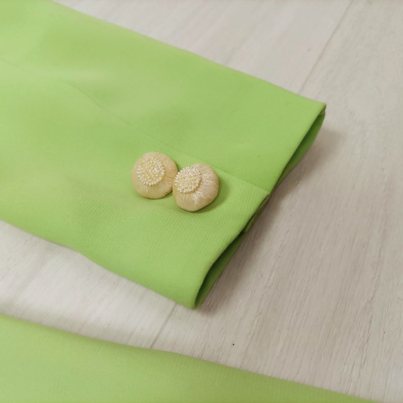 May include: Close-up of a lime green blazer with two white pearl-like buttons on the cuff.