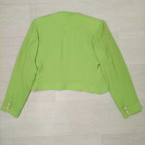 May include: A bright green blazer with long sleeves and gold buttons. The blazer is cropped and has a simple design.