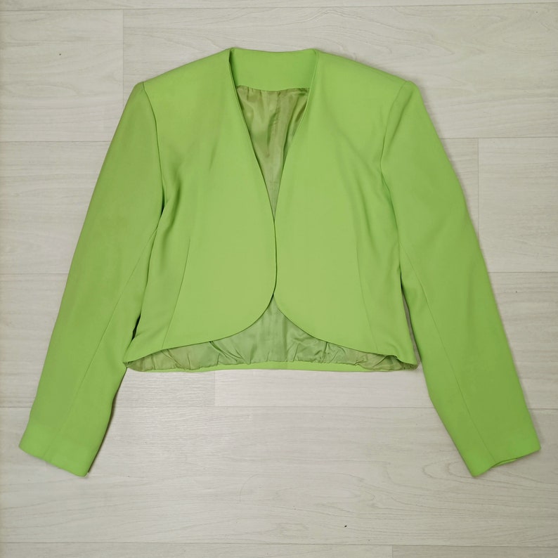 May include: A bright green cropped blazer with long sleeves and a rounded, curved hem.