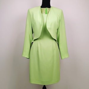 May include: A light green dress suit with a matching jacket and skirt. The jacket has a shawl collar and the skirt is knee-length.