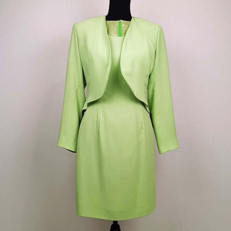 May include: A light green dress suit with a matching jacket and skirt. The jacket has a shawl collar and the skirt is knee-length.