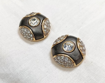 Könnte beinhalten: Ein Paar runde Ohrringe in Schwarz und Gold mit klaren Strasssteinen. Die Ohrringe haben ein geometrisches Design.