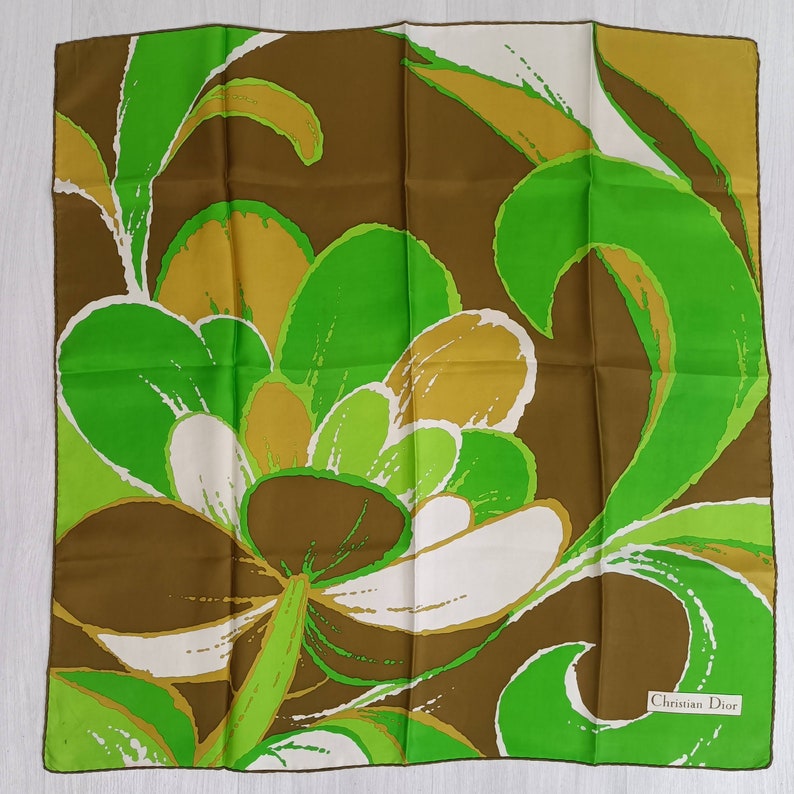 Op de afbeelding: Een groene, bruine en witte zijden sjaal met een abstract bloemenmotief. De sjaal heeft een label met de tekst "Christian Dior".