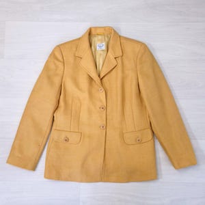 Può includere: Blazer giallo senape dal design classico e sartoriale. Presenta revers a lancia, chiusura a tre bottoni e due tasche frontali. Il blazer ha maniche lunghe e una fodera colorata chiara. Un capo in stile vintage.