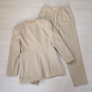Puede incluir: Un traje de dos piezas beige, compuesto por una blazer y un pantal&oacute;n a juego. La blazer tiene un cuello cl&aacute;sico y cierre de botones. El pantal&oacute;n es de corte recto. El traje est&aacute; hecho de una tela texturizada.
