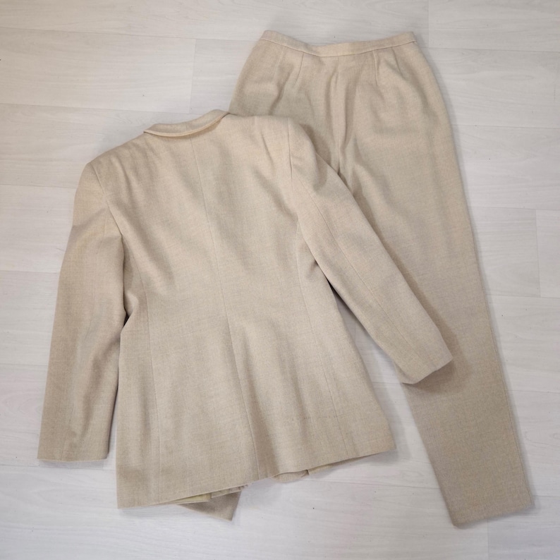 Puede incluir: Un traje de dos piezas beige, compuesto por una blazer y un pantal&oacute;n a juego. La blazer tiene un cuello cl&aacute;sico y cierre de botones. El pantal&oacute;n es de corte recto. El traje est&aacute; hecho de una tela texturizada.